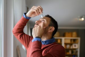 Man applying eye drops for chronic dry eye, possibly in need of corrective surgery.